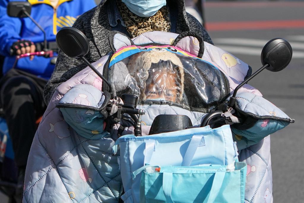 10月18日,一位小朋友在电动自行车的挡风后面躲风。新华社记者 鞠焕宗 摄