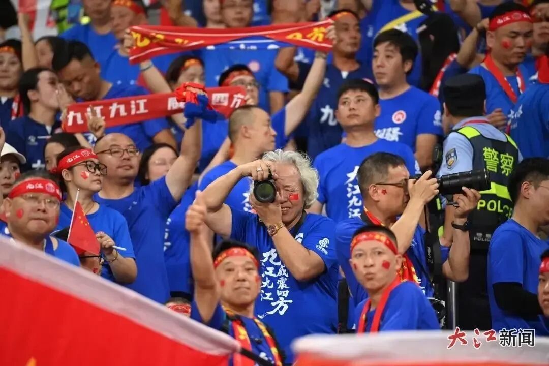 10月4日,两位摄影爱好者在赣超半决赛的球迷方阵中拍摄。江西日报全媒体记者 杨继红 摄