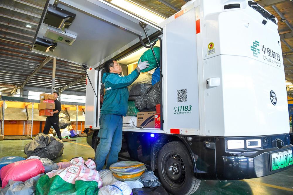 工作人员正在往无人配送车内放置邮件，准备送至乡镇快递共享中心