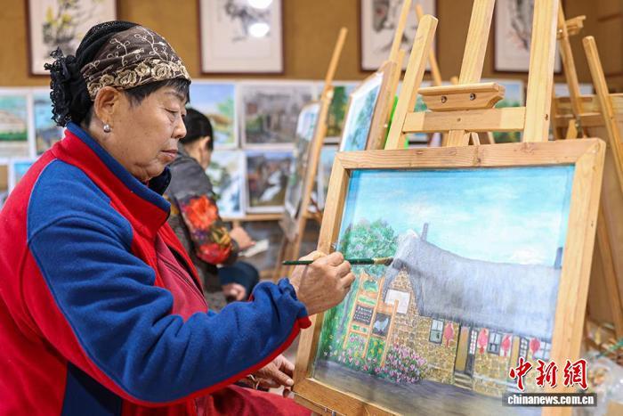 11月19日，“渔家画嫂”在山东荣成牧云庵村的画室里创作，画中的石头房是该村的特色景观。李信君 摄