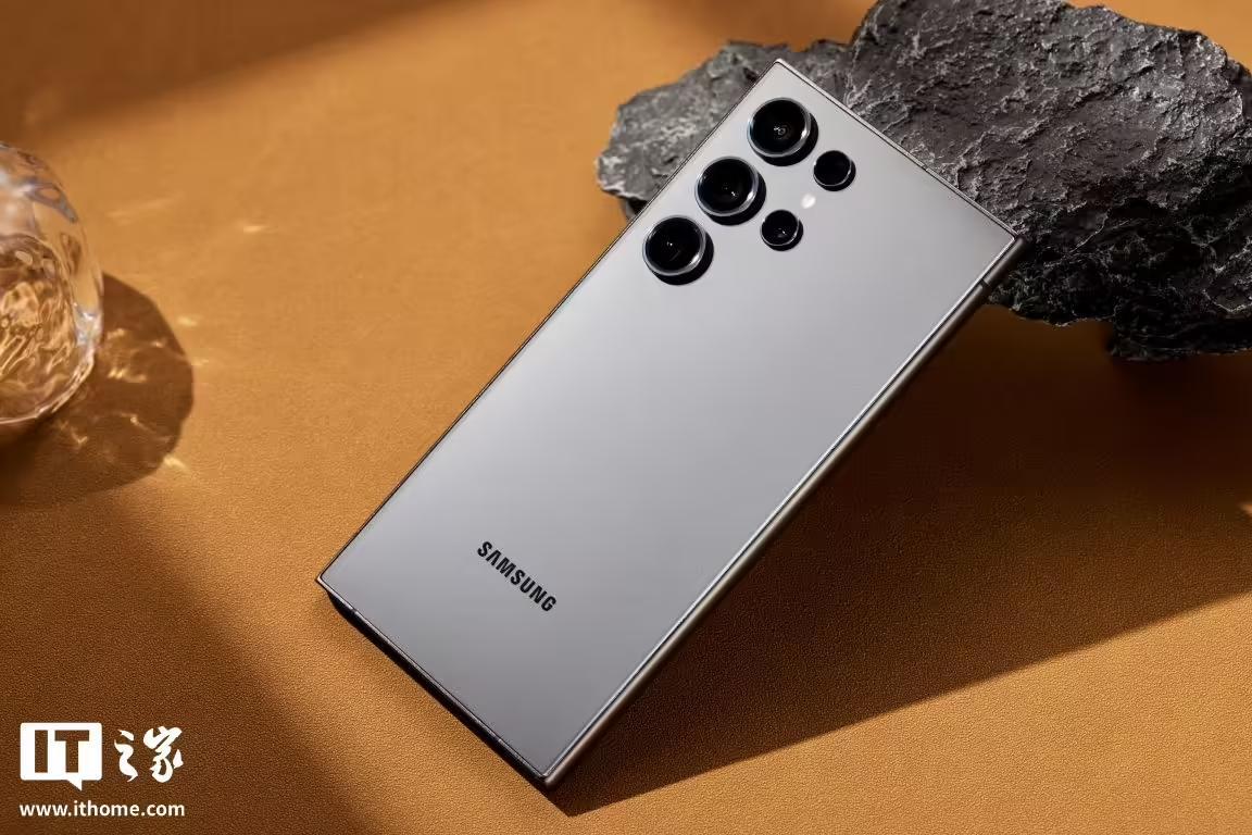 三星Galaxy S24 Ultra黑色款手机背面，展示品牌标识和摄像头模组，放置在带有岩石和玻璃装饰的背景上。