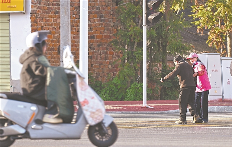 11月27日，在莲花县妇幼保健院附近，文明劝导志愿者帮助行动不便的老人过马路。