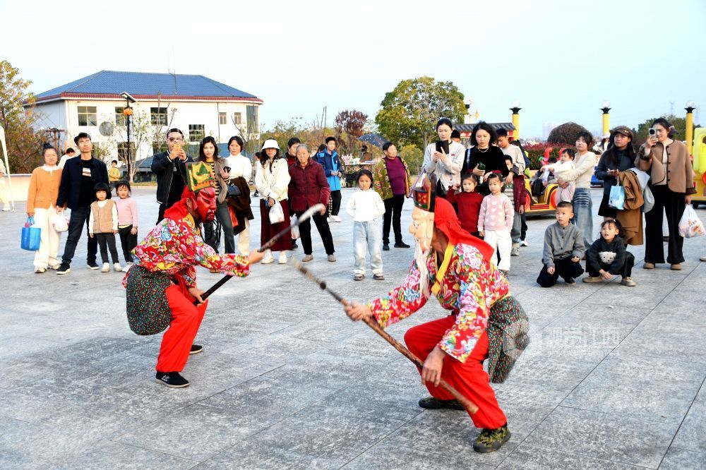 2025年12月7日下午,江西省抚州市南丰县蜜桔湖景区橘子餐厅广场,傩师们在跳傩祈福,吸引省内外游客们驻足观看、拍照,游客们还拿着傩面具拍照留念。