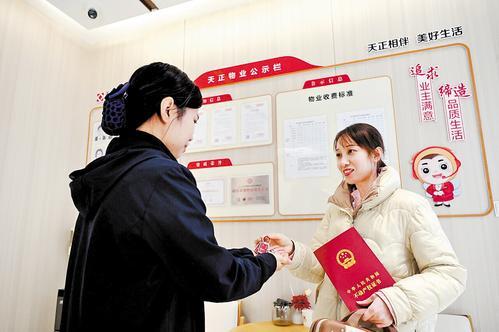 11月25日,衡水市区山河玺院一区物业服务中心,一名业主(右)在领取新房钥匙的同时拿到了不动产登记证书。