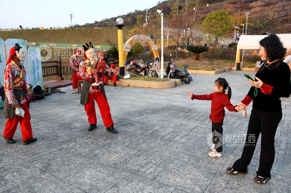2025年12月7日下午,江西省抚州市南丰县蜜桔湖景区橘子餐厅广场,傩师们在跳傩祈福,吸引省内外游客们驻足观看、拍照,游客们还拿着傩面具拍照留念。