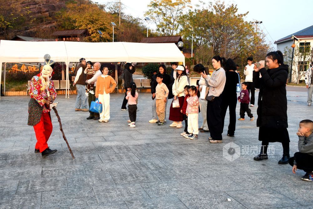 2025年12月7日下午,江西省抚州市南丰县蜜桔湖景区橘子餐厅广场,傩师们在跳傩祈福,吸引省内外游客们驻足观看、拍照,游客们还拿着傩面具拍照留念。