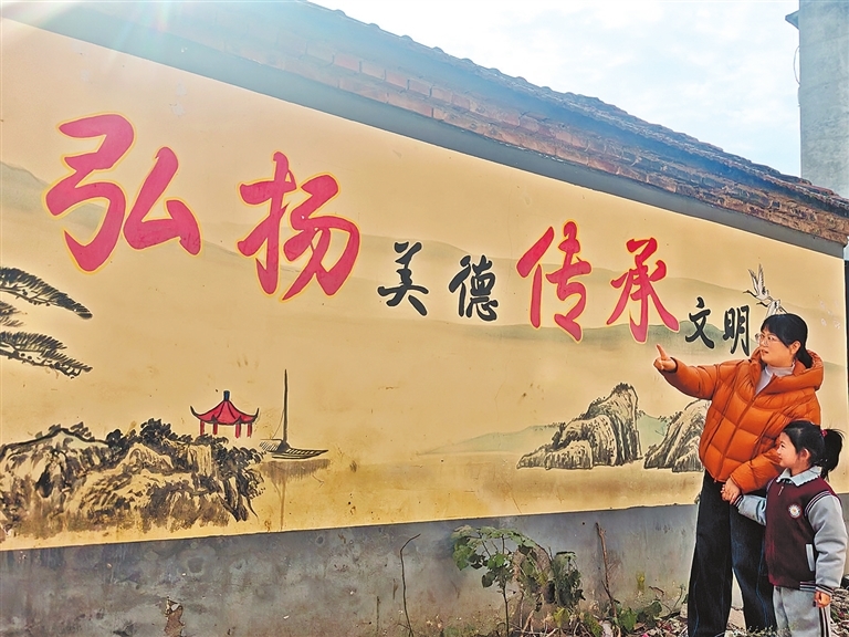 12月4日,鹿邑县卫真街道四新居委会,一位年轻的妈妈正给孩子讲解文化墙上的内容。 郭凯 摄