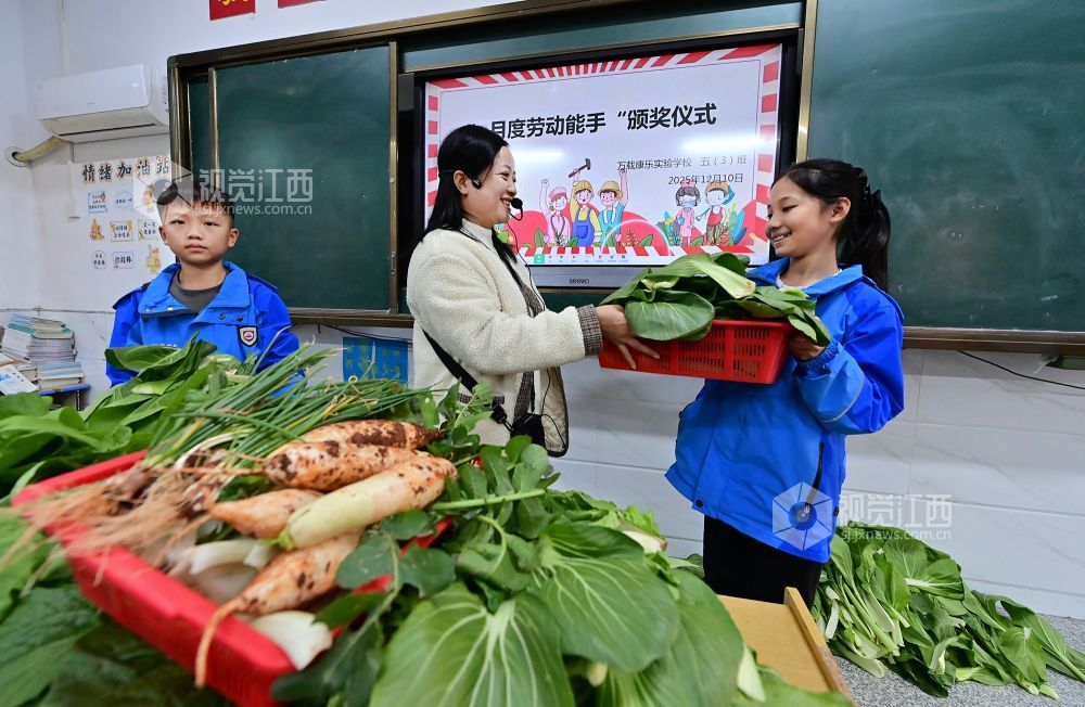 2025年12月10日，江西省宜春市万载县康乐实验学校的老师在“月度劳动能手”颁奖仪式上给学生奖励蔬菜，让学生体会劳动的光荣。