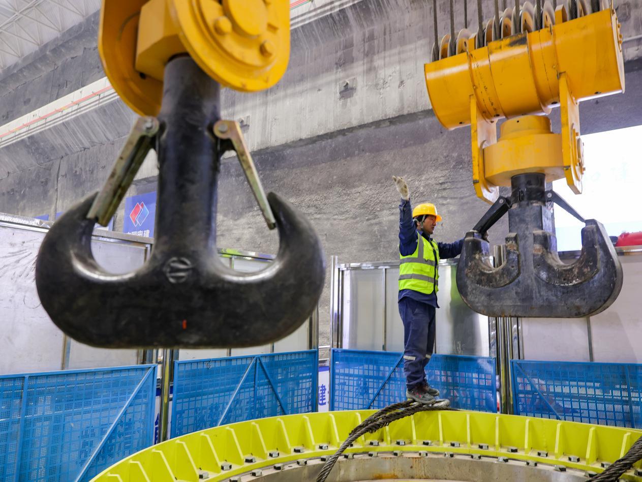 鲁山豫能抽水蓄能电站地下厂房内，巨型起重吊钩下，建设者精准指挥机组吊装作业，勾勒出能源工程建设的动人剪影。摄影：郭东伟