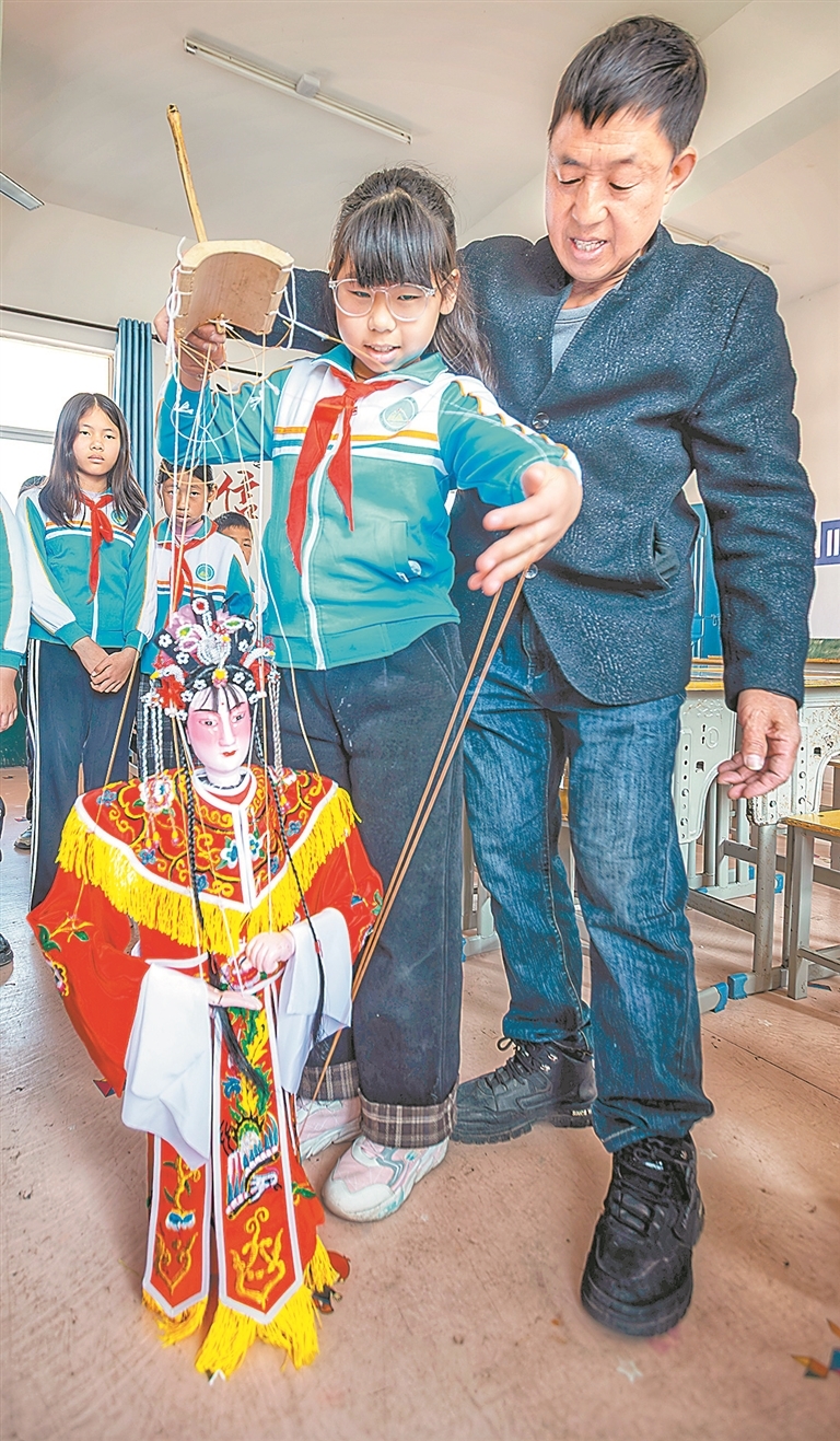 在广昌县塘坊中心小学，谢帮银让孩子们亲手触摸木偶、尝试拉线，在他们心中播下文化传承的种子。