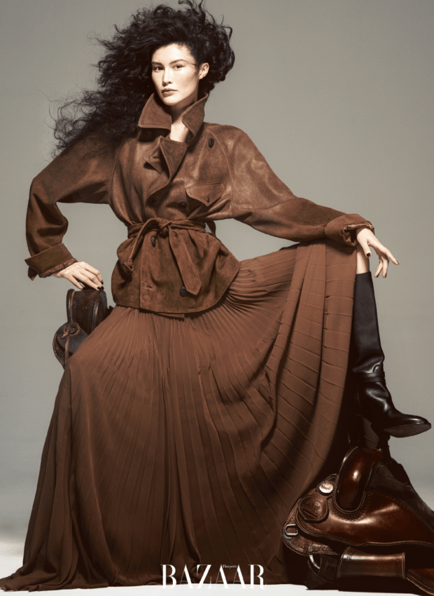 何穗棕调风衣搭同色系长裙，单手轻掀裙摆的姿态灵动优雅。