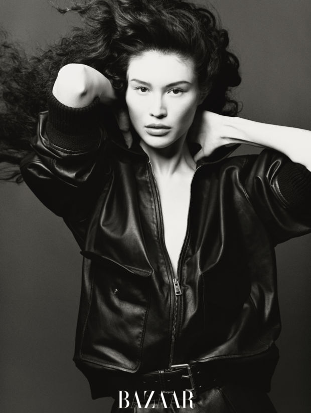 何穗黑皮外套造型，抬手轻抵颈肩的姿态慵懒松弛。