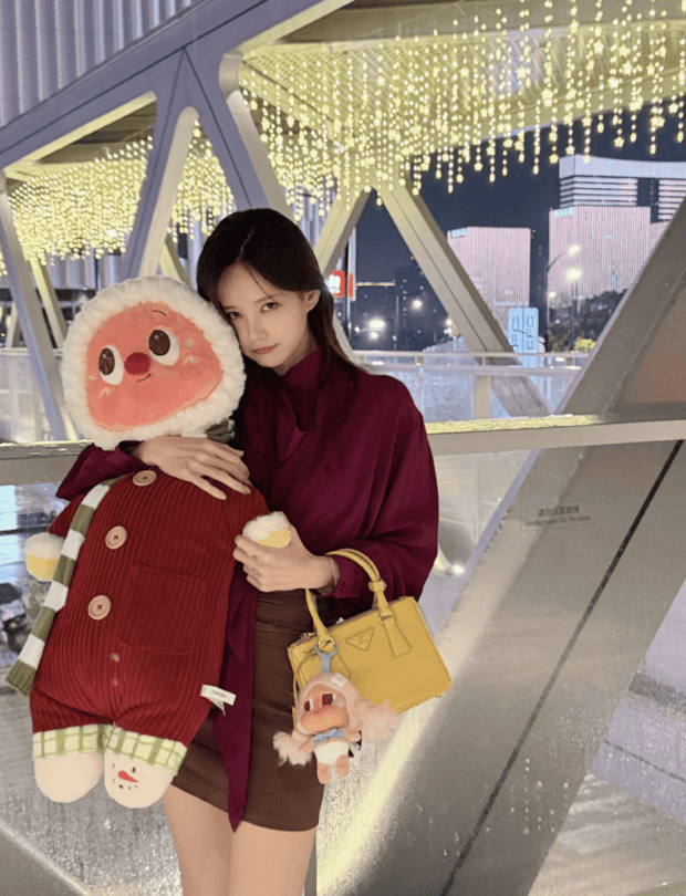 李一桐穿酒红色上衣，亲昵抱着圆萌玩偶。
