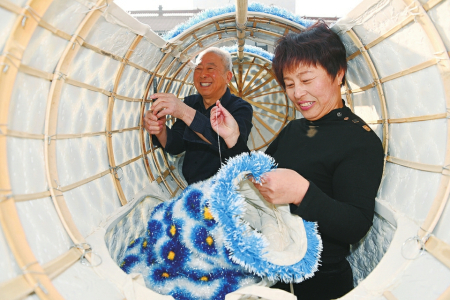 王成林（后）向王娟传授麒麟兽腿的缝合技巧，将传统民俗技艺倾囊相授。