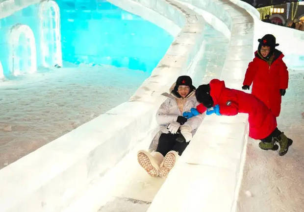 胡杏儿登上冰做成的滑梯,两个小孩在身旁陪着她。