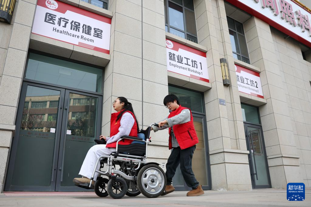 AI训练师王娜娜(右)推着马凤珍从兰州市心连心社会工作服务中心残疾人就业工坊前经过,准备前往餐厅吃午餐(1月14日摄)。新华社记者 陈斌 摄