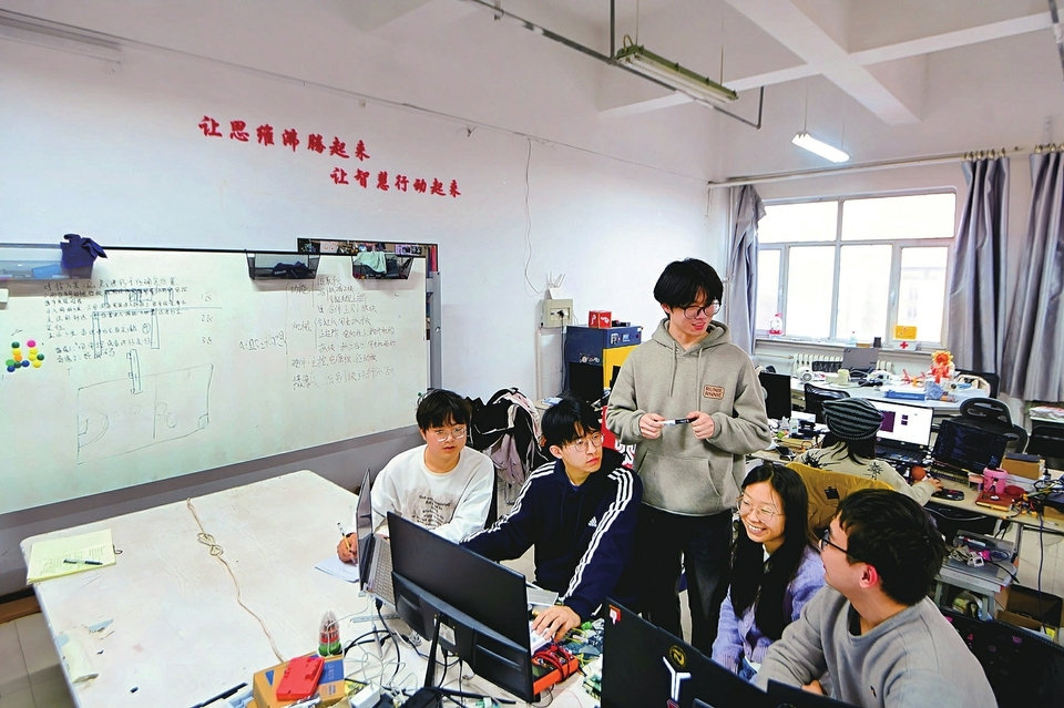 ROBOCON工作室内，2025赛季冠军队成员童志杨（中）与新赛季成员进行竞赛思路交流与经验分享。