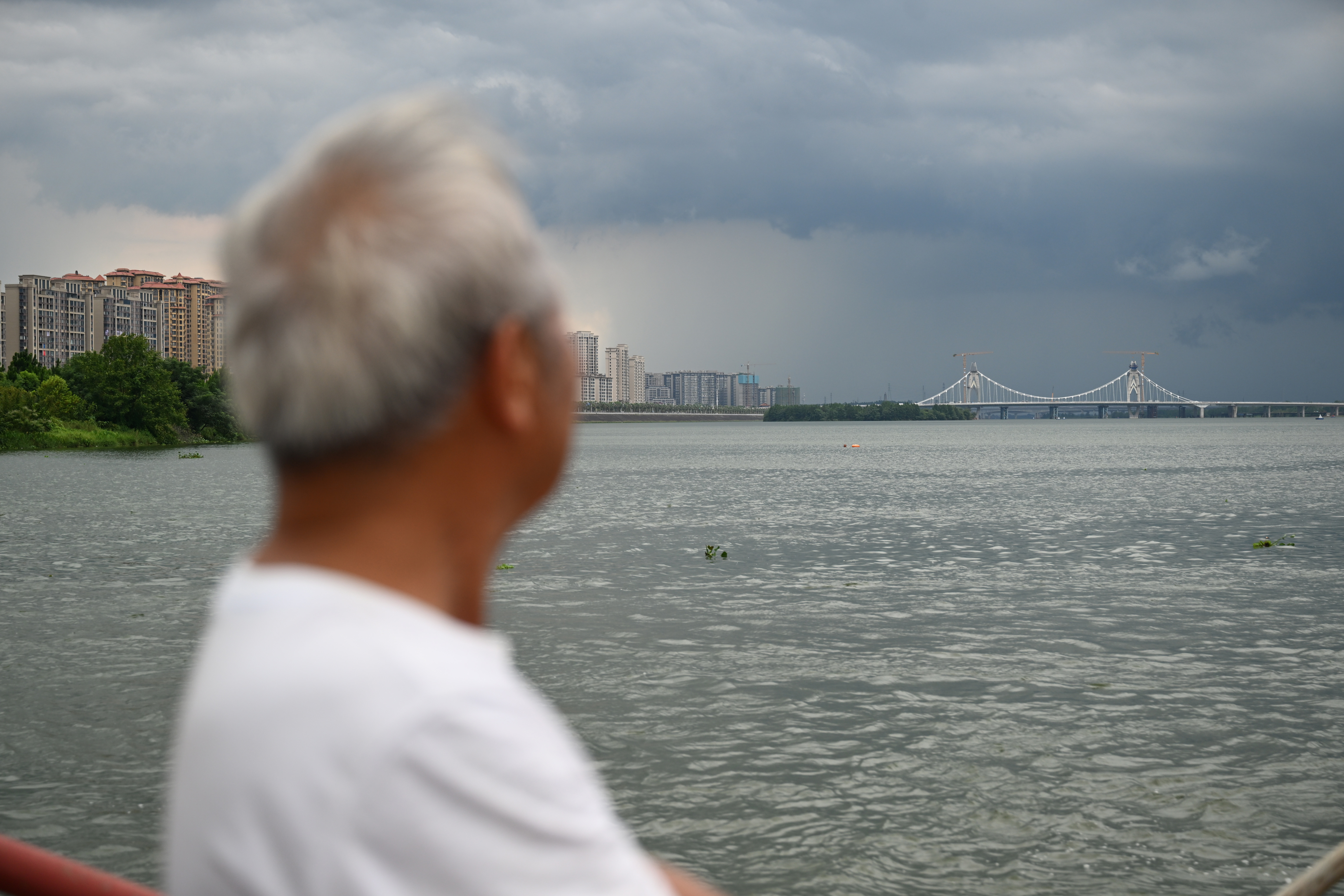 ▲2025年7月30日,泰和县永昌渡口的老渡工在渡船上望向正在建设中的澄江大桥。