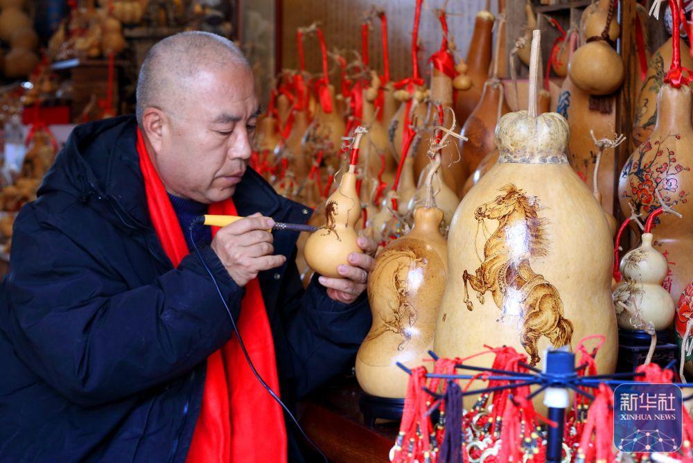 1月17日,在青岛市即墨区,市级非物质文化遗产代表性传承人黄旭在创作马题材的葫芦烙画。新华社发(梁孝鹏 摄)