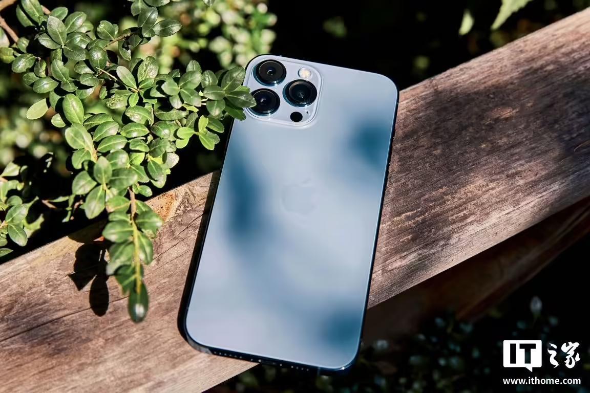 iPhone 13 Pro Max的背面特写,放置在户外木质栏杆上,背景有绿植。