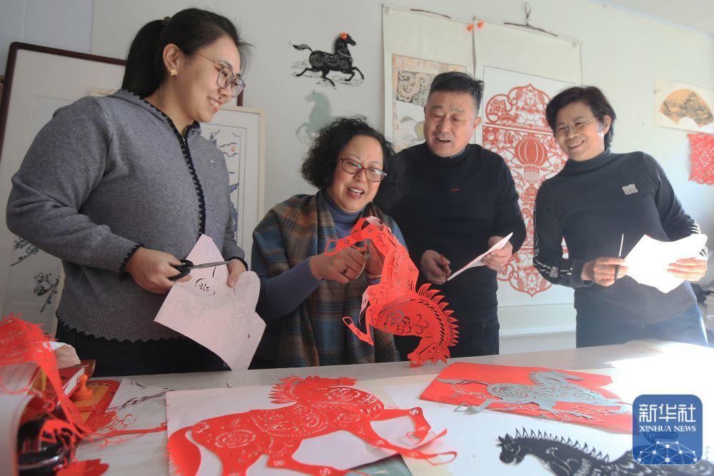 1月22日,在山东省荣成市石岛管理区港湾街道文化活动室,剪纸艺人刘秋白(左二)向剪纸爱好者讲解马的剪纸技巧。新华社发(王福东 摄)