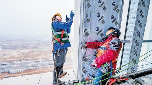 雄安新区启动区财富大厦项目施工现场，施工人员正在百米高空进行幕墙工程铝板单元体安装作业。