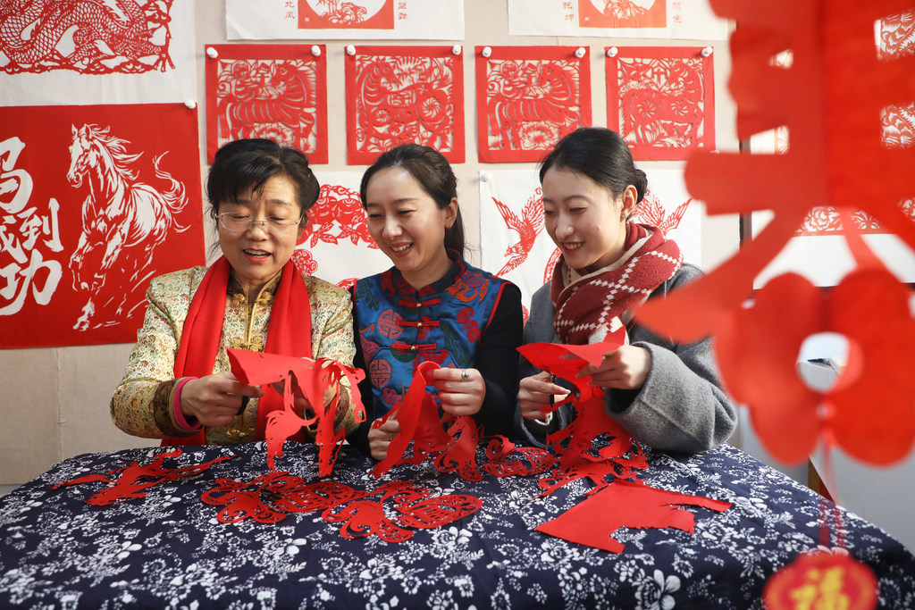 2月10日，唐山市丰润区太平路街道冀新社区，剪纸艺人葛英（左一）在教居民创作生肖马剪纸作品。
