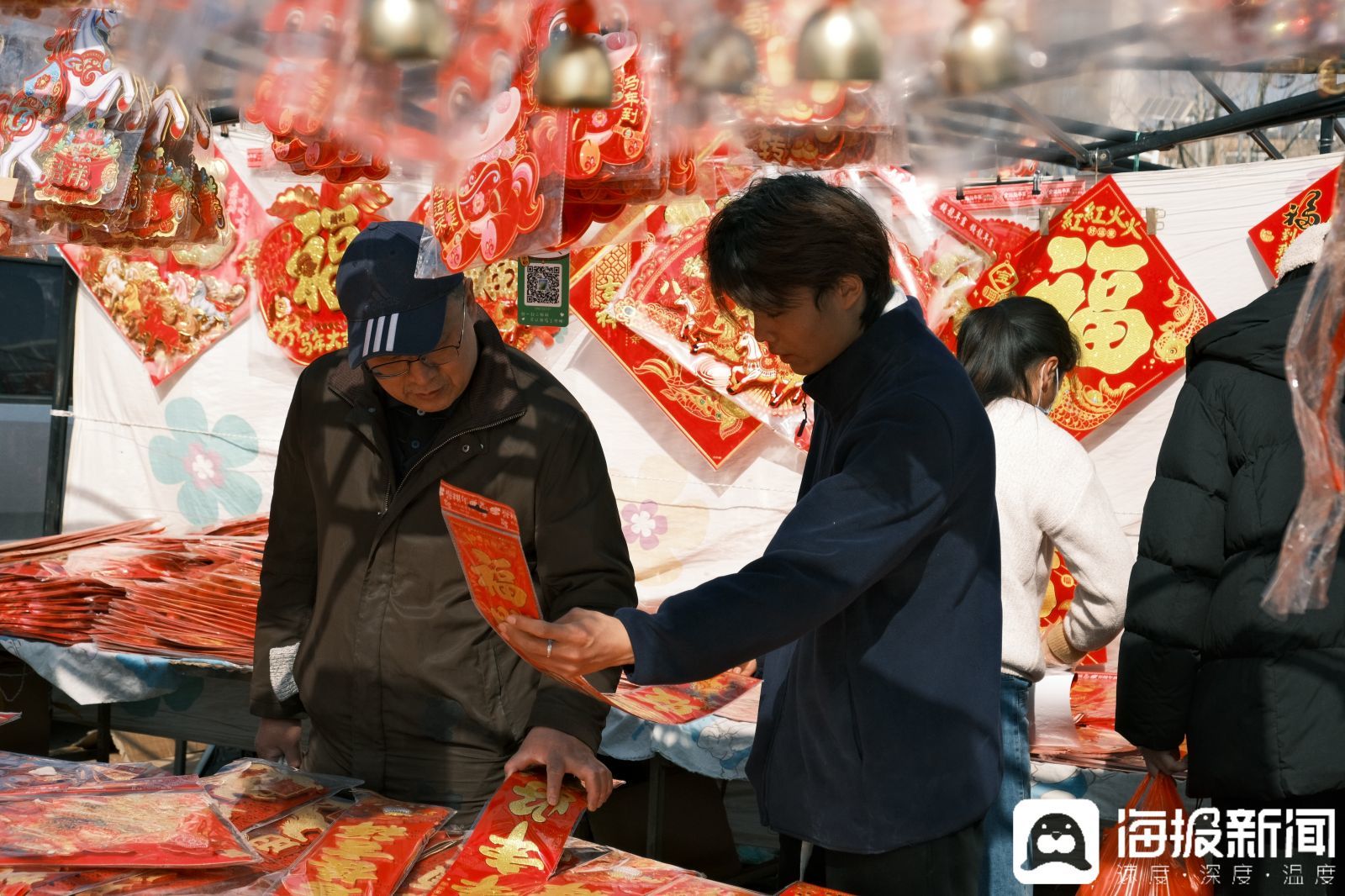 一位略显腼腆的年轻人正帮家里照看摊位，给顾客介绍年货。