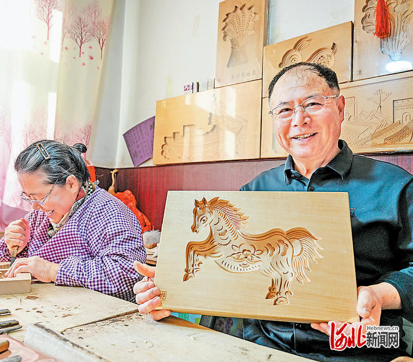 2月3日,省级非遗黄骅面花模子雕刻技艺代表性传承人高殿华(右)展示雕刻设计的马年主题面花模子。