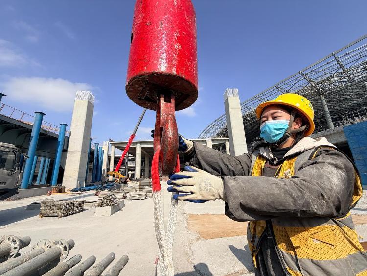 2月25日，在济南遥墙机场二期改扩建工程施工现场，建筑工人正在配合吊机进行作业。新华社记者 张钟仁 摄