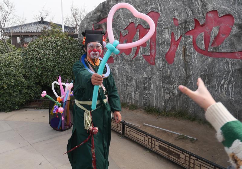 小丑演员吹气球和游人互动。