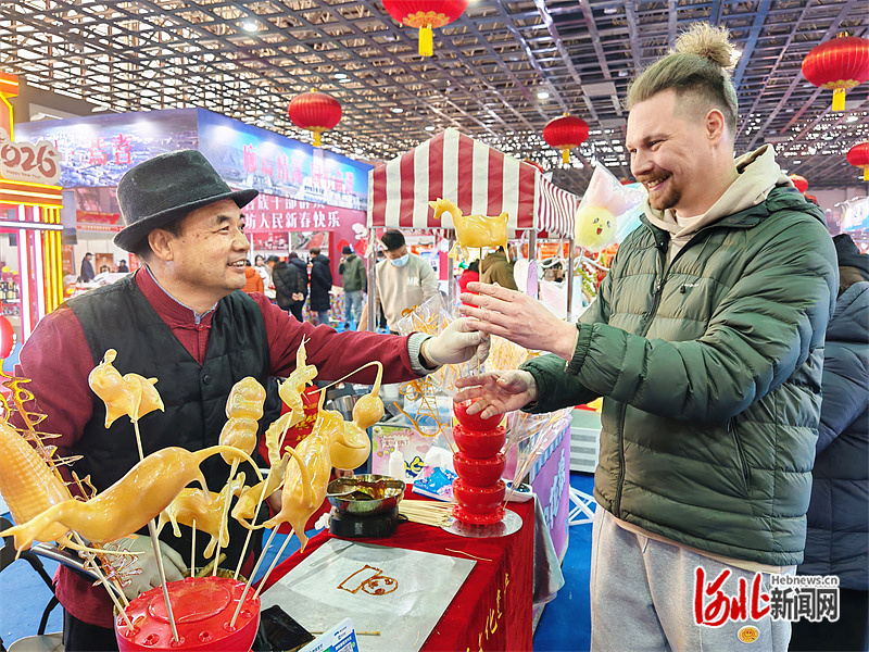 2月10日，在廊坊国际年货节现场，尼古拉（右）近距离体验非遗吹糖人技艺。河北日报记者 刘杰 摄