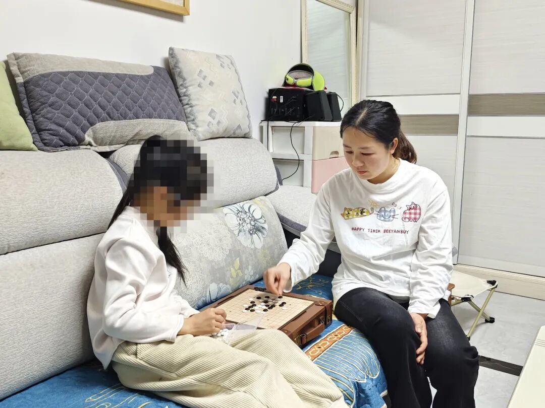 杨晓梅坐在沙发上陪女儿下棋
