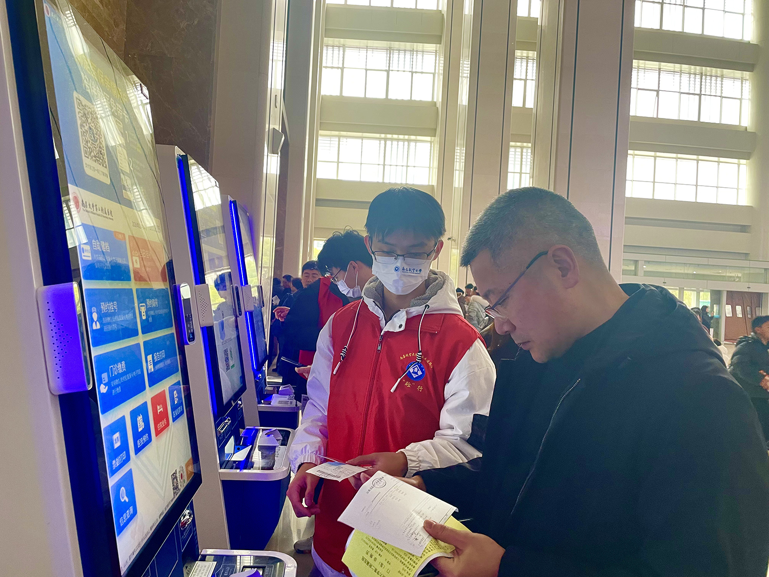 ▲身着红马甲的志愿者正在医院引导患者就诊、协助挂号分诊。