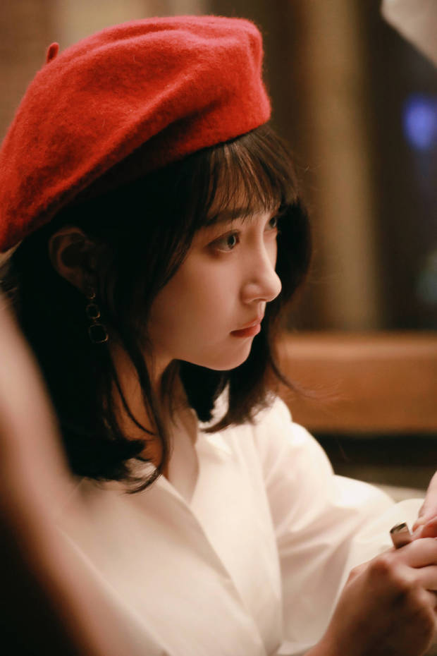 关晓彤头戴红色贝雷帽,身着白衬衫,侧眸凝视,在暖光中尽显温柔文艺的气质。