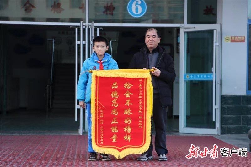金昌市实验小学春季开学典礼上，失主朱德权为谢鹏轩赠送锦旗。