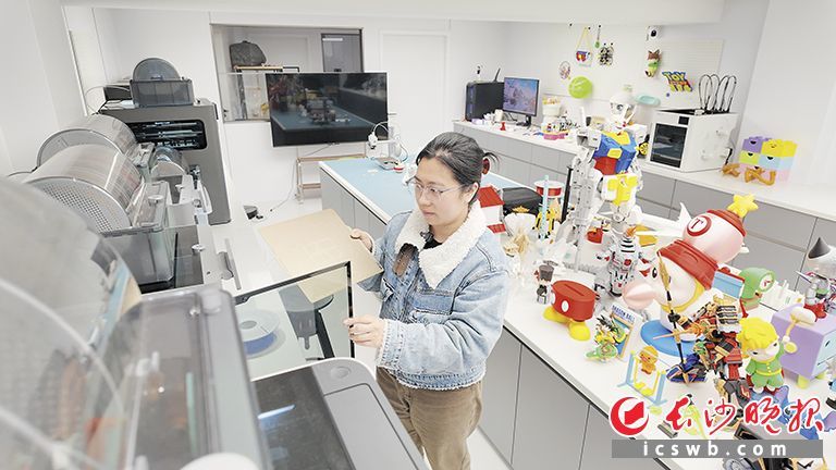 “打哒打3D造物社”主理人周雅仪正在工作，旁边是3D打印的各种玩具摆件。长沙晚报全媒体记者 曾灵 摄