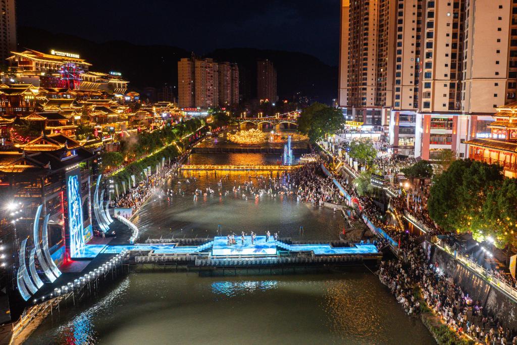 2025年7月19日，市民和游客在湖北省宣恩县城贡水河畔观看文化表演（无人机照片）。新华社发（陈绪开摄）
