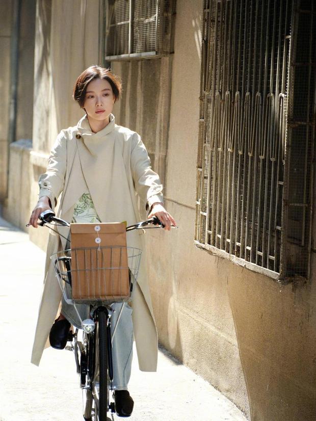 倪妮骑车穿行，风衣造型文艺随性。