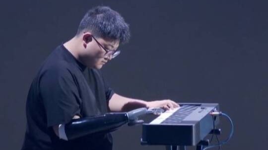强脑科技创始人韩璧丞展示智能仿生手，佩戴者借助它现场弹奏乐曲