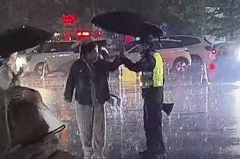安徽阜阳颍上一学校门口，巡防队员冒雨护学，市民看到后，上前为其撑起雨伞