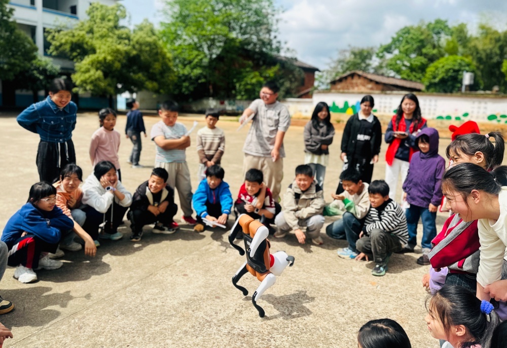 近日，在江西省抚州市东乡区珀玕中小学，科普志愿者正与学生一起观看机器狗表演。