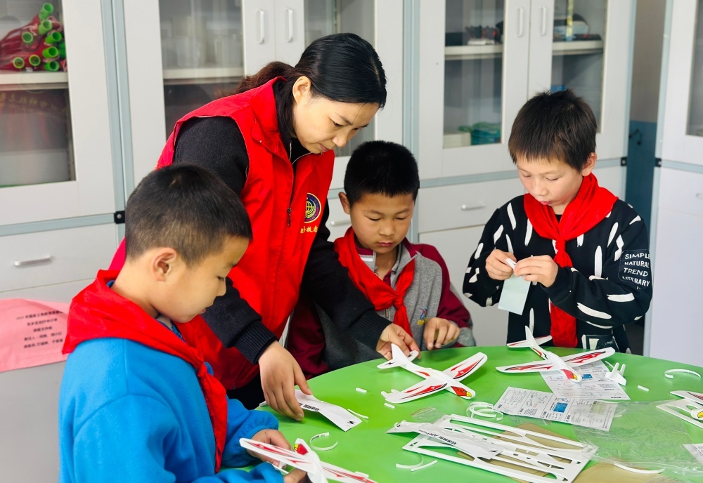 近日，在江西省抚州市东乡区珀玕中小学，科普志愿者正与学生制作手工飞机模型。