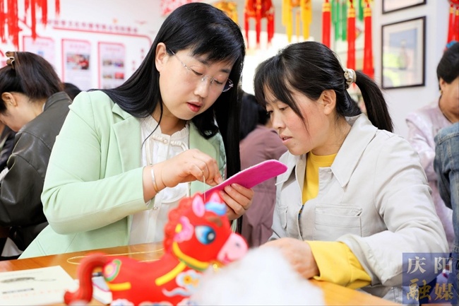 任艳艳（左）为绣娘示范香包刺绣基本绣法