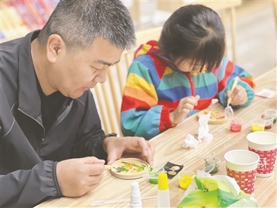 图为社区居民正在细致勾勒精致纹样，耐心涂抹各色釉料。