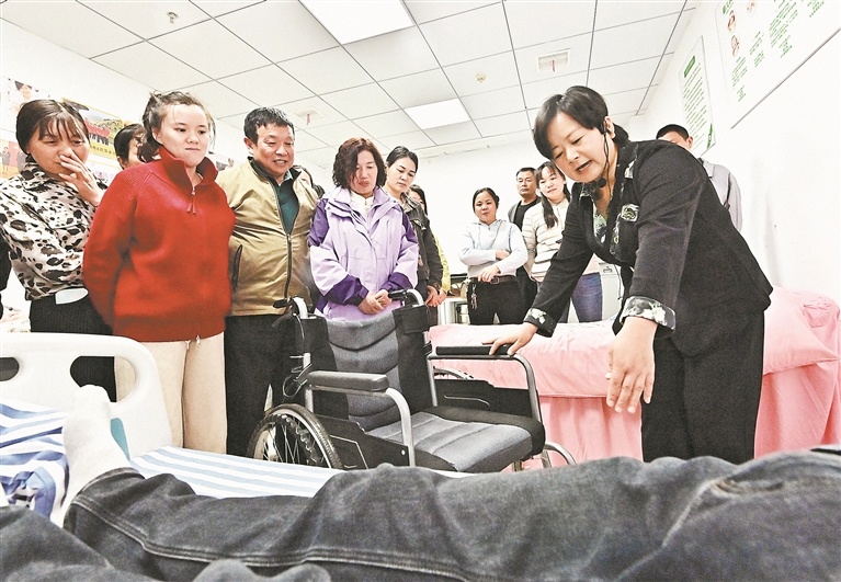 4月21日，养老护理实操现场，陈英俯身指导学员为老年人翻身。