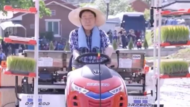 李在明戴着草帽挂着毛巾，开插秧机体验种水稻