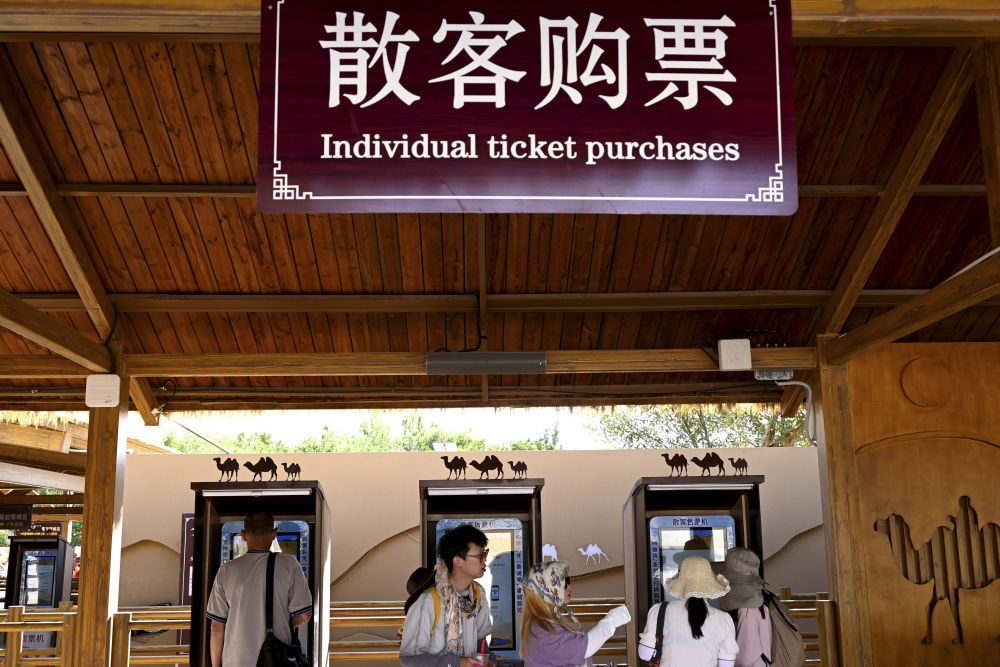 5月31日,敦煌市鸣沙山月牙泉景区骆驼乘骑区,游客在散客售票机上购票。