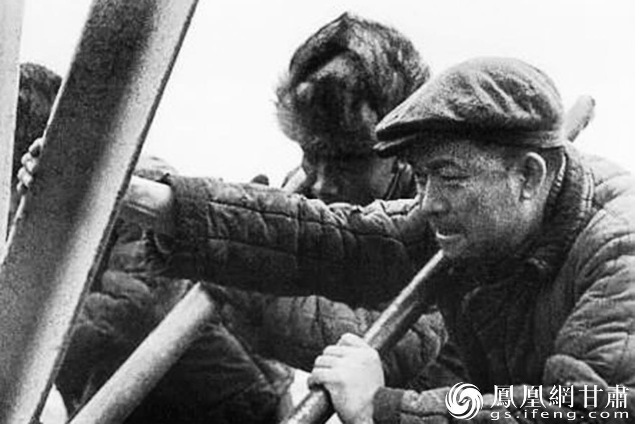 王进喜（右）奋力向上扛设备　资料图片