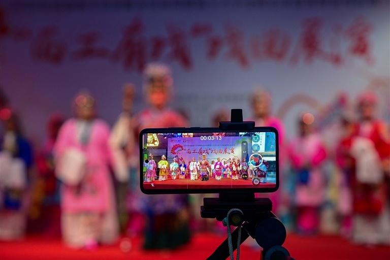 在洛阳市西工小街，河洛本土戏曲名段轮番上演，观众架起手机拍摄精彩片段。李卫超 郜大鹏 摄